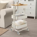 White rolling cart with bamboo top, holding a mug, cookies, and a magazine. Clear bins hold items on lower shelves.