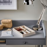 Gray desk with organized compartment tray for pens and notes, wicker box, and adjustable chrome lamp.