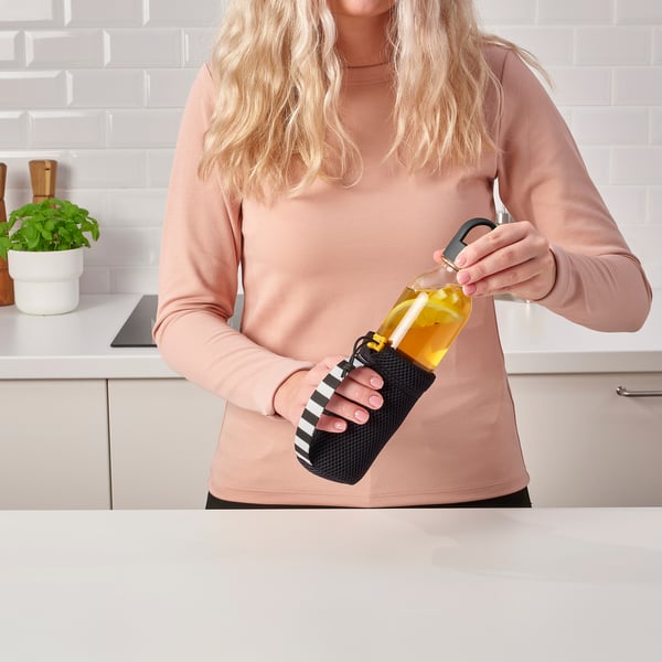 Woman holding a black mesh bottle carrier by its handle, holding a yellow bottle with a straw.