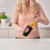 Woman holding a black mesh bottle carrier by its handle, holding a yellow bottle with a straw.