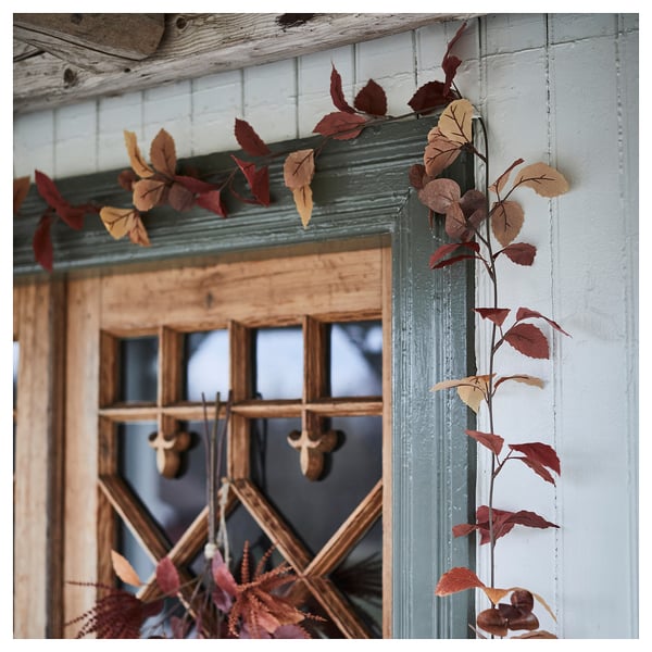 Lush autumn garland in warm reds and golds elegantly draped on a rustic wooden window, showcasing quality craftsmanship and vibrant colors.