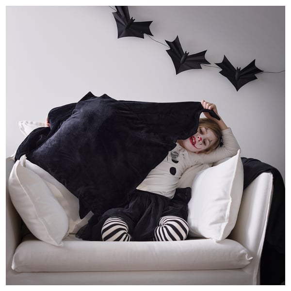 Child lying on couch, covered with black bat-shaped blanket, smiling, with white and black striped socks.
