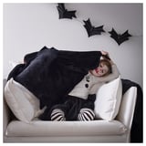 Child lying on couch, covered with black bat-shaped blanket, smiling, with white and black striped socks.