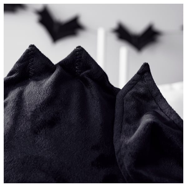 Close-up of black fleece bat-shaped pillow cover with stitched details, soft texture visible, zipper partially open.