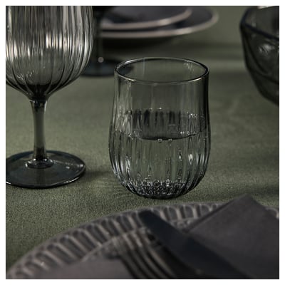 Two elegant, ridged glasses on a green tablecloth. One holds a small amount of water.