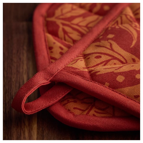 Folded red kitchen mitt with orange patterns, laid on a wooden surface. Durable stitching and loop for hanging visible.