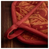 Folded red kitchen mitt with orange patterns, laid on a wooden surface. Durable stitching and loop for hanging visible.