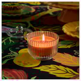 A lit HÖSTAGILLE candle in a fluted jar with a lid, emitting a sandalwood, patchouli, and fir scent.