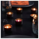 Six lit tealights on a dark surface, creating a warm, cozy glow. One tealight emits a soft pink hue. Their pleasant vanilla scent fills the room.