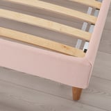 This image shows a corner view of an upholstered bed frame with a sloping headboard and wooden slats, designed for comfort and easy cleaning.