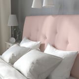 A cozy bed with a light pink headboard and white pillows, providing comfortable reading support with classic design and upholstery.
