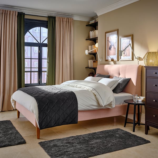 Bedroom with IDANÄS pink bed, dark quilt, white pillows, curtains, wooden furniture, floor rugs, and window view.