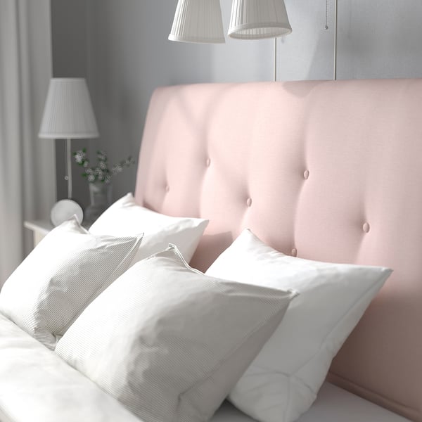 A cozy bedroom with a light pink upholstered bed frame, white pillows, and bedside lamps. The sloping headboard provides back support.