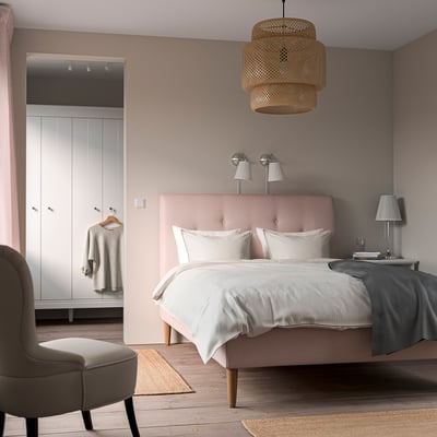 Pink IDANÄS bed with sloping headboard, flanked by lamps, with pendant light and side chair. Adjacent closet with clothes.