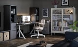 Modern home office with IDÅSEN desk, off-white chair, shelves, and computer. Wood floor, dark walls, and books.