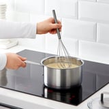 A person whisking cream in a saucepan on a modern stovetop.