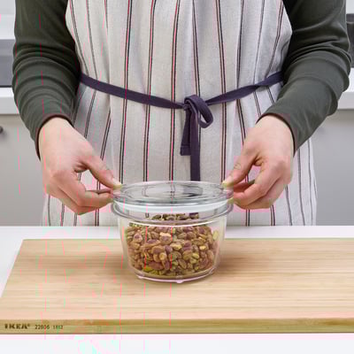 Person wearing an apron placing a jar with mixed nuts on a wooden board.