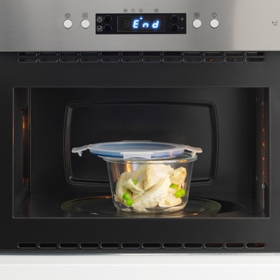 Clear glass container in microwave, showing heated food inside. Digital display reads end above, highlighting oven-safe, leak-proof lid.