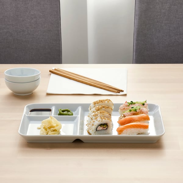 White tray with sushi, soy sauce, chopsticks, and bowls on a table.