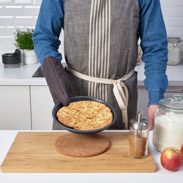 Person holding a baked dessert in a non-stick pie dish on a wooden board.
