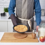 Person holding a baked dessert in a non-stick pie dish on a wooden board.