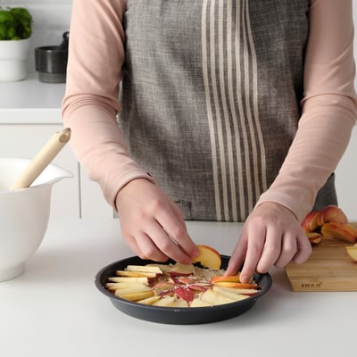 Person prepares apple slices in a black pie dish with a non-stick coating for baking.