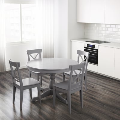 Round extendable dining table with 4 chairs, leaf stored underneath, near modern kitchen with oven.