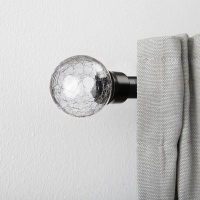 Clear, round glass finial with crackled design on curtain rod, holding light grey curtain.