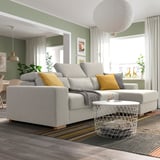 Modern living room with large grey ISTABY sectional sofa, yellow pillows, white coffee table, striped rug, large window, and plants.
