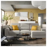 Modern living room with large gray ISTABY sectional sofa, yellow pillows, wooden coffee table, white lamp, and large plants.