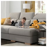 Girl drawing on ISTABY sofa, teddy bear, lamp, books.