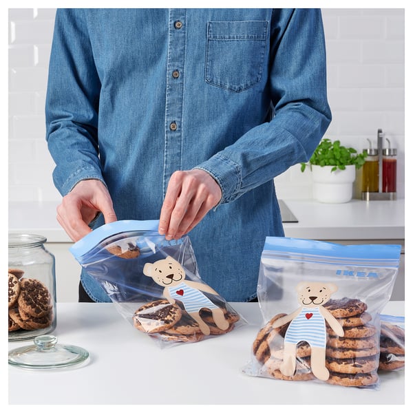 A person in a denim shirt is handling clear blue resealable bags with bear designs labeled IKEA filled with cookies.