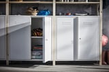 White IVAR cabinets in garage, one open revealing tools and accessories, sturdy metal and pine design with shelves.