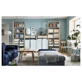 Modern living room with blue couch, gray ottoman, wooden shelves full of books and decorative items, large window, and blue walls.