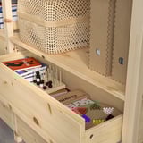 Wooden bookshelf with adjustable shelves, holding books and colorful game pieces in drawers.
