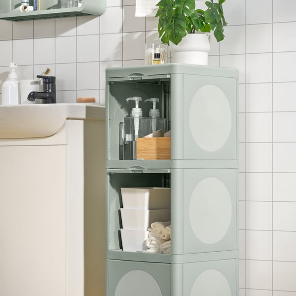 Green IVÖSJÖN bathroom cabinet storing bottles, towels, and a plant.