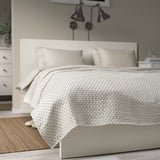 Off-white bedspread with dark grey stitching on a large bed,part of a minimalist bedroom setup.