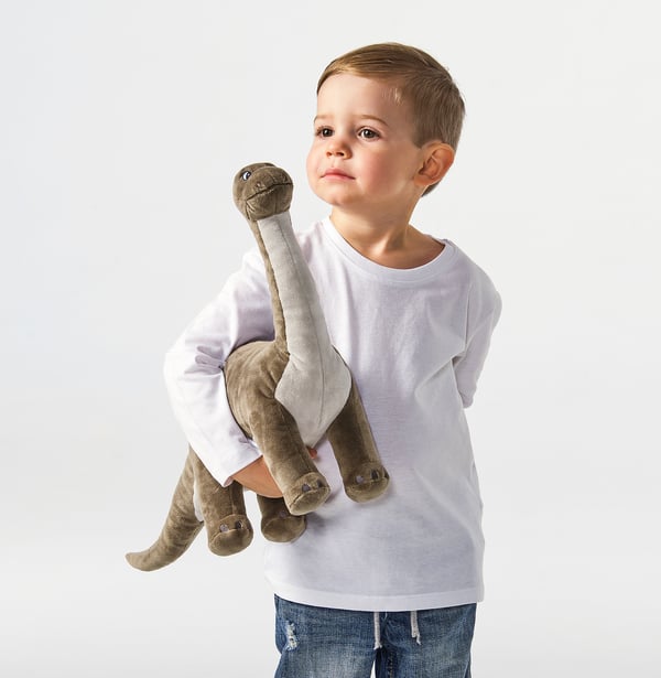 A young boy holds a cuddly brontosaurus stuffed animal, designed for comfort and play, suitable for ages 12 months and up.