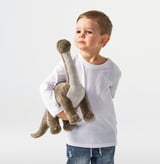 A young boy holds a cuddly brontosaurus stuffed animal, designed for comfort and play, suitable for ages 12 months and up.