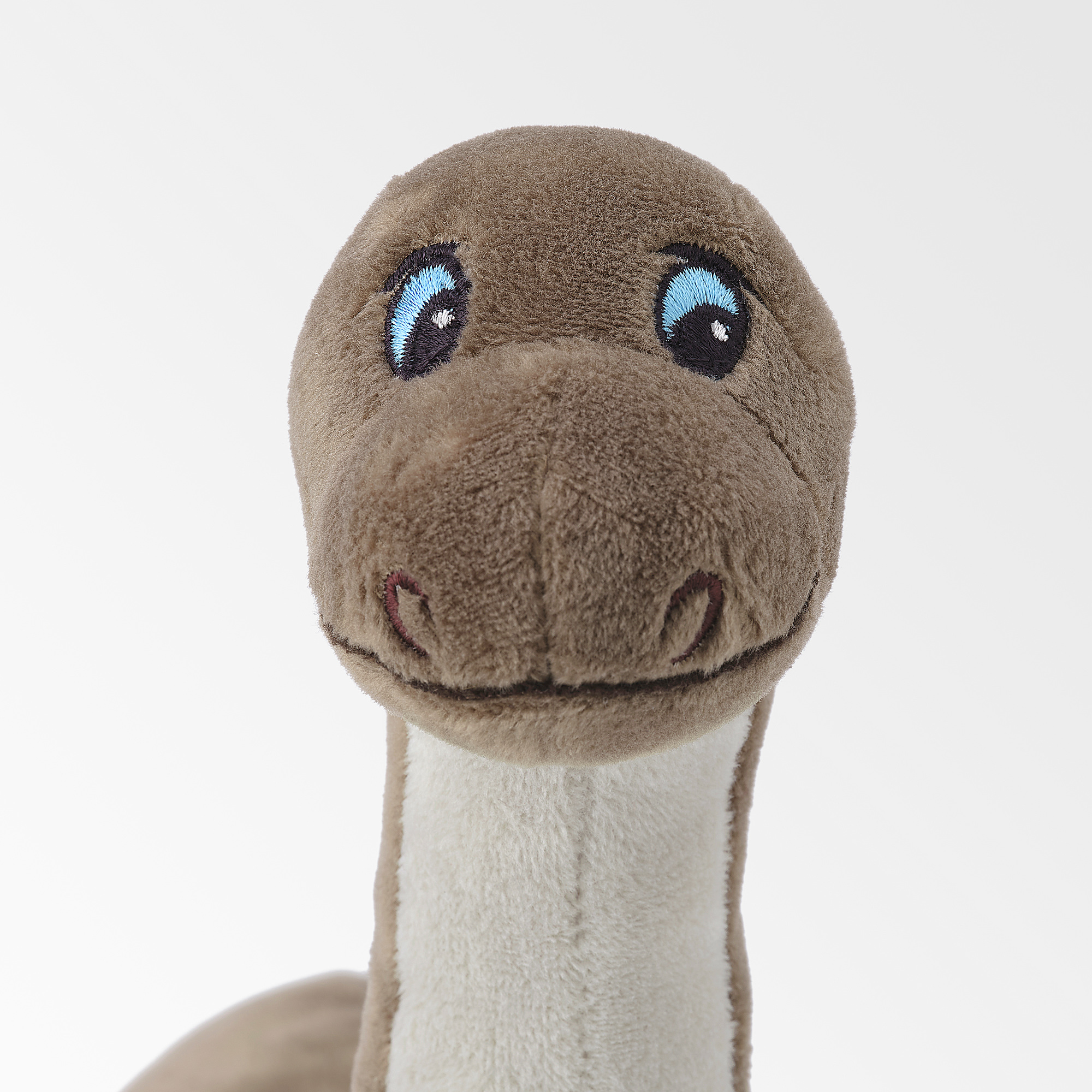 Stuffed dinosaur toy with light brown body, white underbelly, blue eyes, and stitched smile, showcasing quality craftsmanship.
