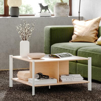 Modern living room with JÄTTESTA bamboo coffee table, white legs. Green sofa, decorative vase, books, and headphones. Clean, sleek design.
