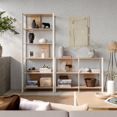 Modern, light beige living room with light wood shelves filled with books and decor. Abstract art and natural elements.