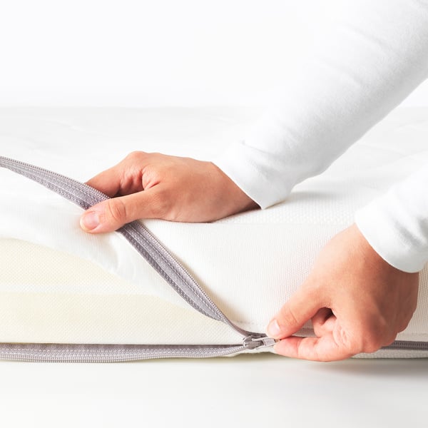 Image shows hands zipping up a cot mattress for easy cleaning.