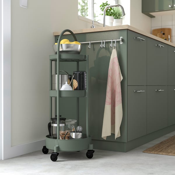 Modern grey-green JUTTERSBO trolley with 3 shelves stocks kitchen essentials, fits neatly beside cabinets.