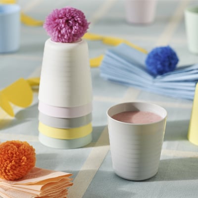 KALAS cups in white, small, round, stackable. Bright pom-poms and napkins decorate table.