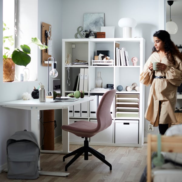 Woman by KALLAX shelf with books, chair, desk, plants.