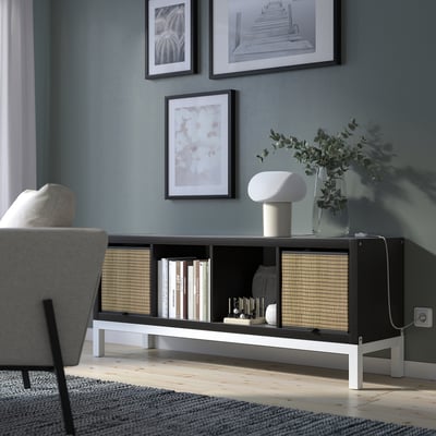 Modern living room with KALLAX black shelving unit, housing books, vases, and a white lamp. Unit contrasts with grey walls and light wood floors.