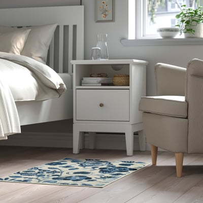 A bedroom with a white KANTLINJE area rug, blue and white, soft underfoot, placed beside a bed and a chair, adding warmth and comfort to the room.