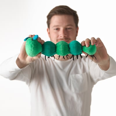 Man holding green, segmented plush toy with legs, likely a musical toy for babies.
