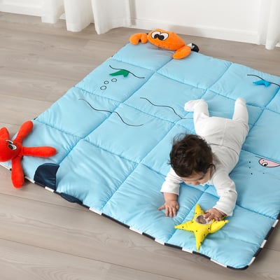 Baby plays on blue sensory mat with plush sea creature toys.